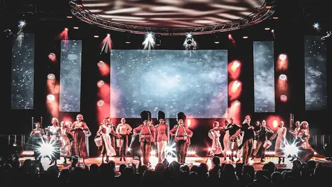 The West End Kids company performing a full-cast number on a large stage, with guards in bearskin hats at the centre