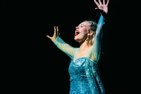 A West End Kids performer singing a solo in an ice-queen costume under a spotlight