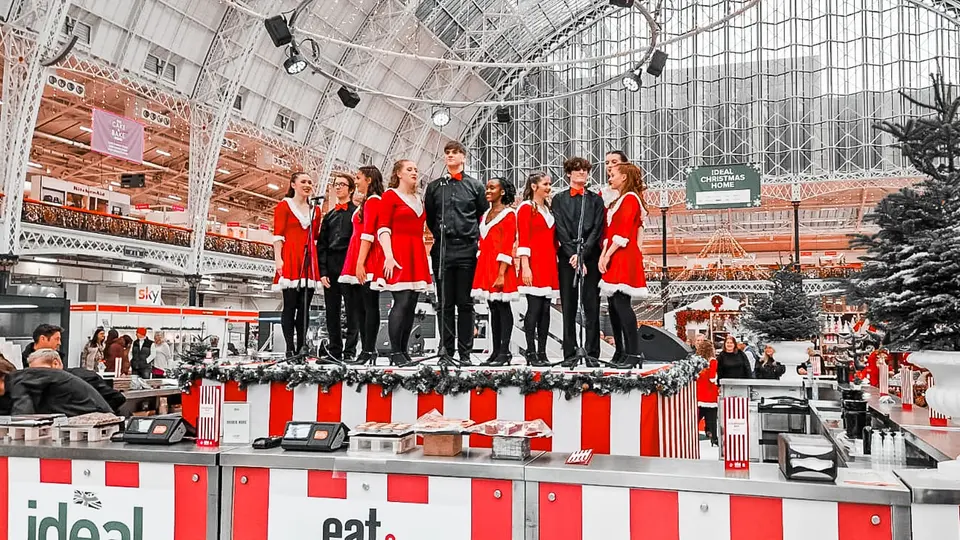 The West End Kids troupe singing in festive costumes on stage at the Ideal Home Show Christmas