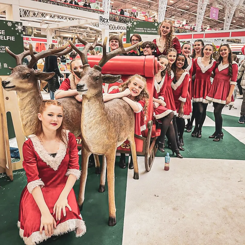 West End Kids performers in festive costumes with model reindeer and a sleigh at the Ideal Home Show