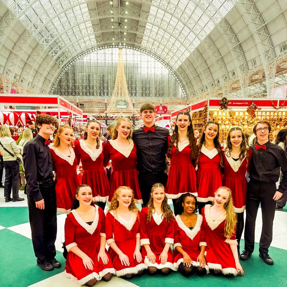 The West End Kids troupe in festive costumes posing for a group photo under the glass roof of an exhibition hall